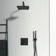 Schwarzes Duschsystem von Ideal Standard mit Regenbrause und Handbrause, montiert an einer hellen Wand. Heizkörperständer links mit Handtuch.